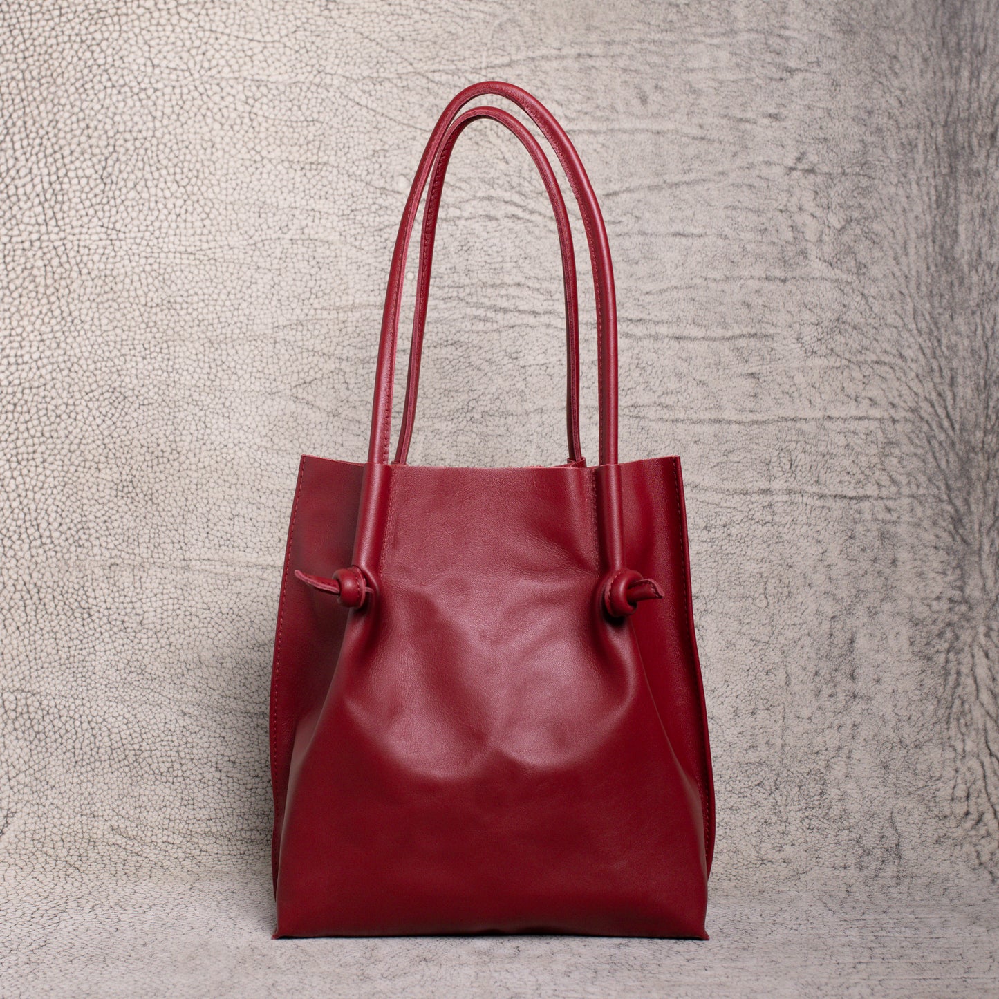 Front-facing view of the Flora Leather Tote in Smooth Calf Burgundy, showcasing its rich artisan leather, dual rolled handles, and minimalist knot detailing.
