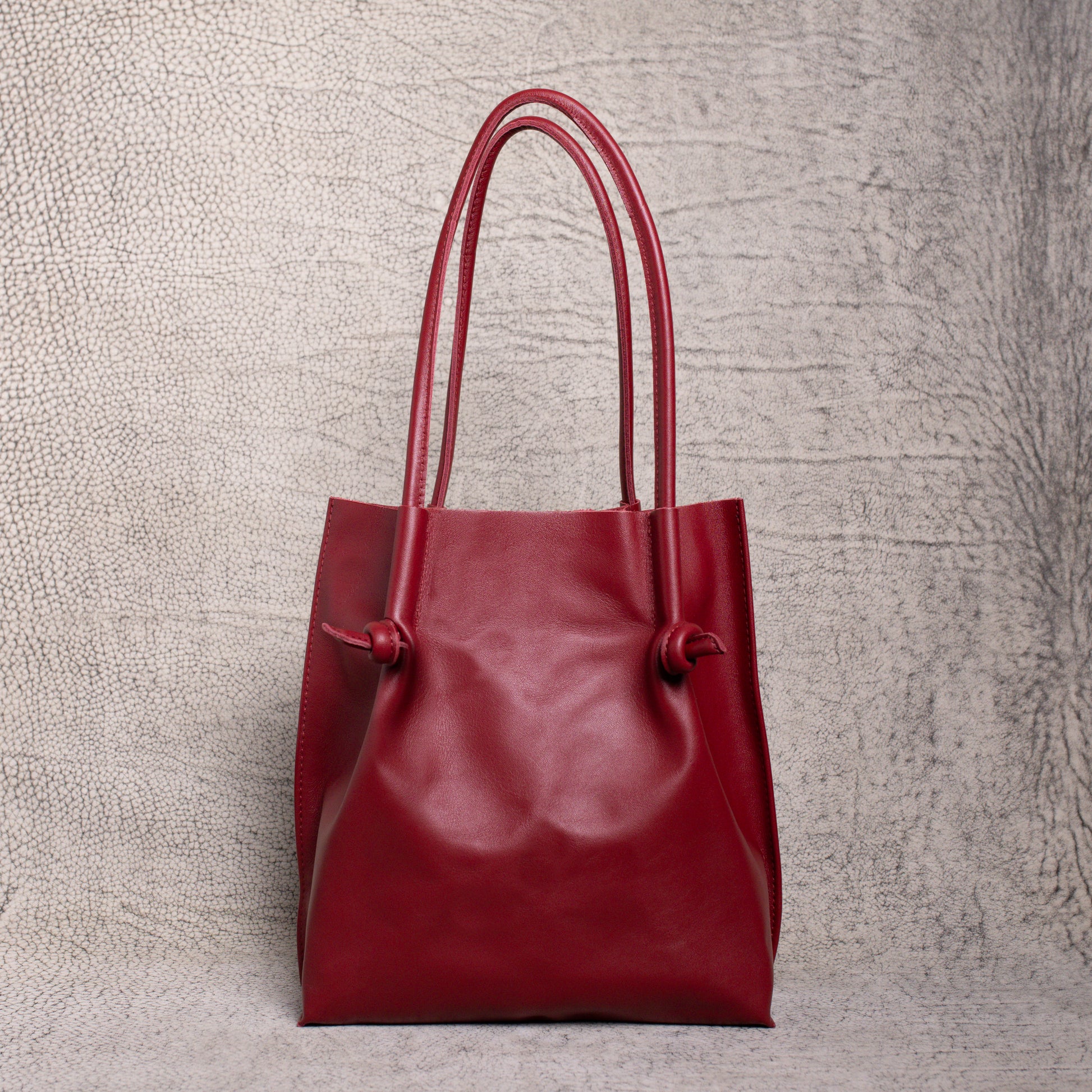 Front-facing view of the Flora Leather Tote in Smooth Calf Burgundy, showcasing its rich artisan leather, dual rolled handles, and minimalist knot detailing.
