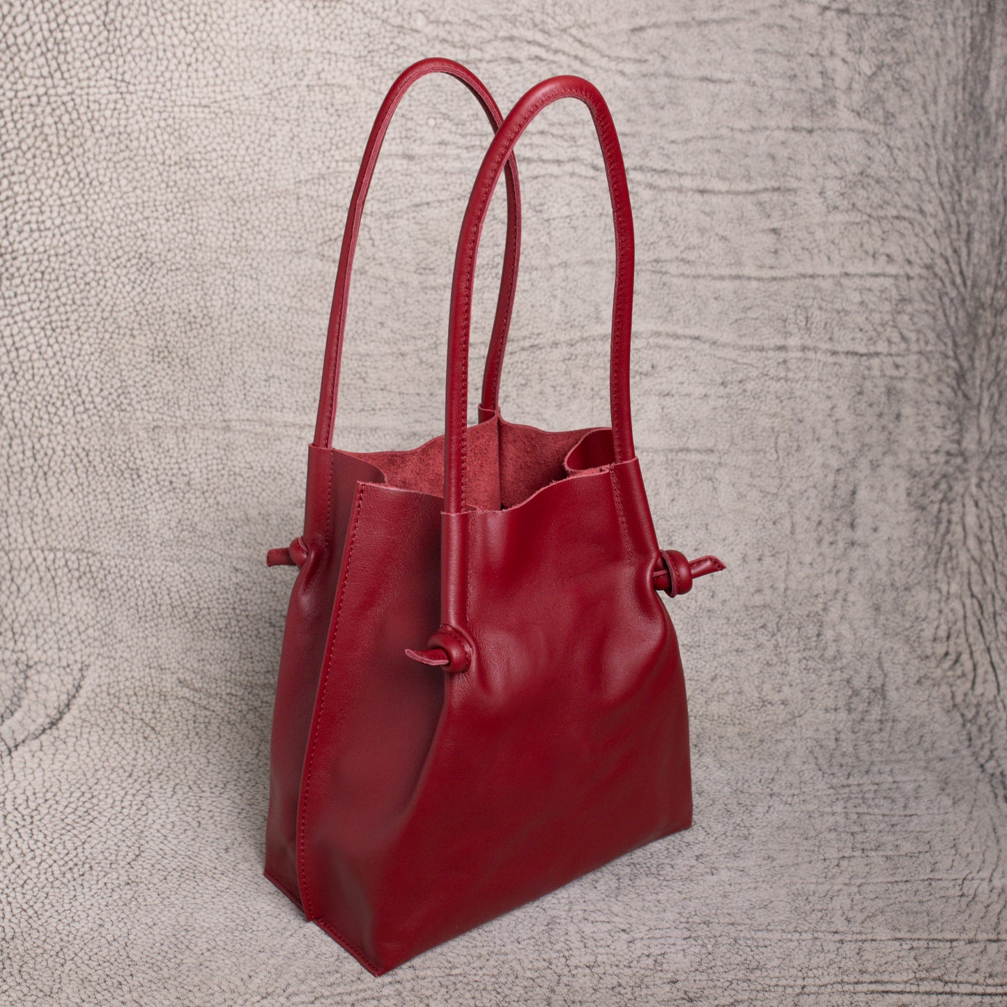 Angled side view of the Flora Leather Tote in Smooth Calf Burgundy, highlighting its spacious open-top design and raw suede interior lining.