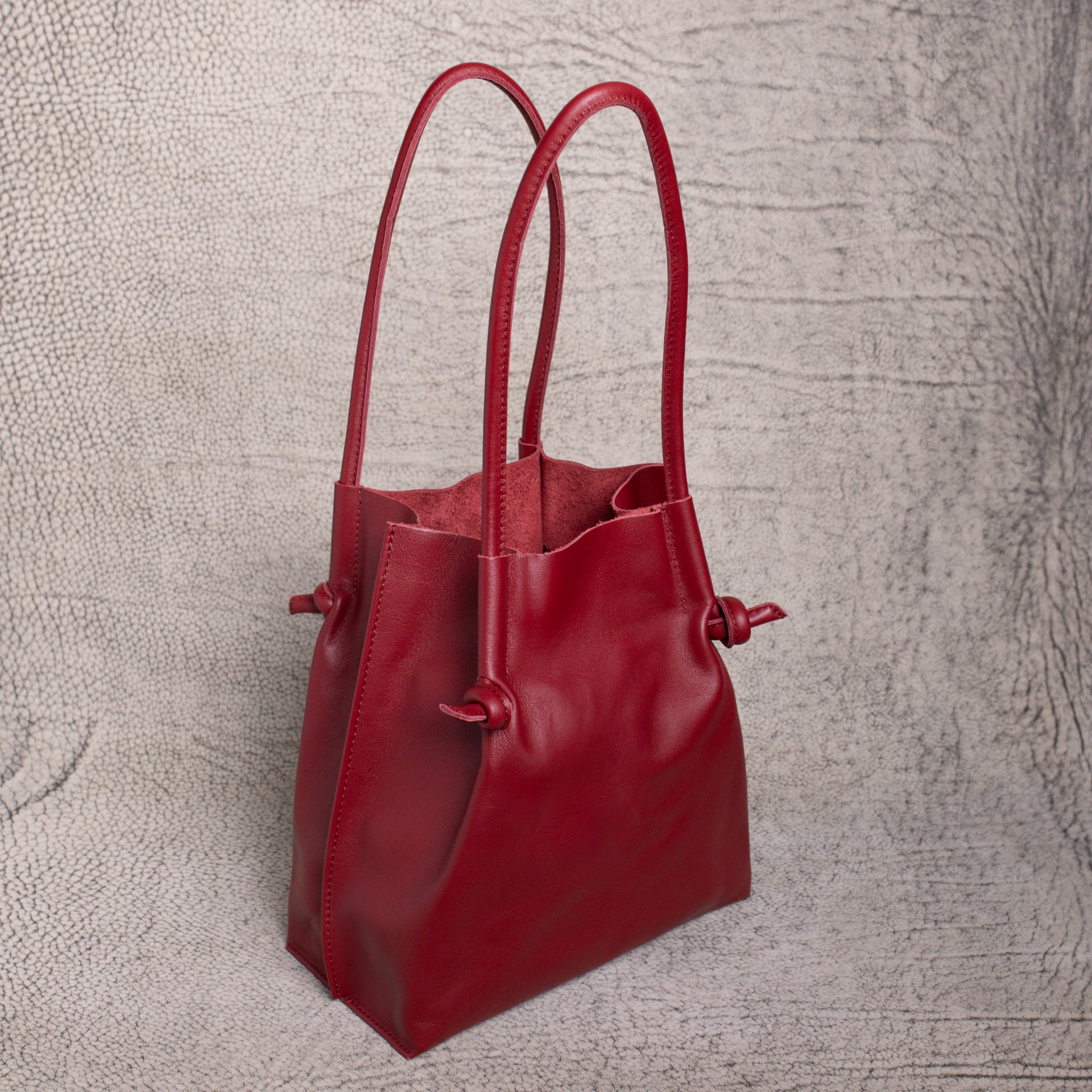 Angled side view of the Flora Leather Tote in Smooth Calf Burgundy, highlighting its spacious open-top design and raw suede interior lining.