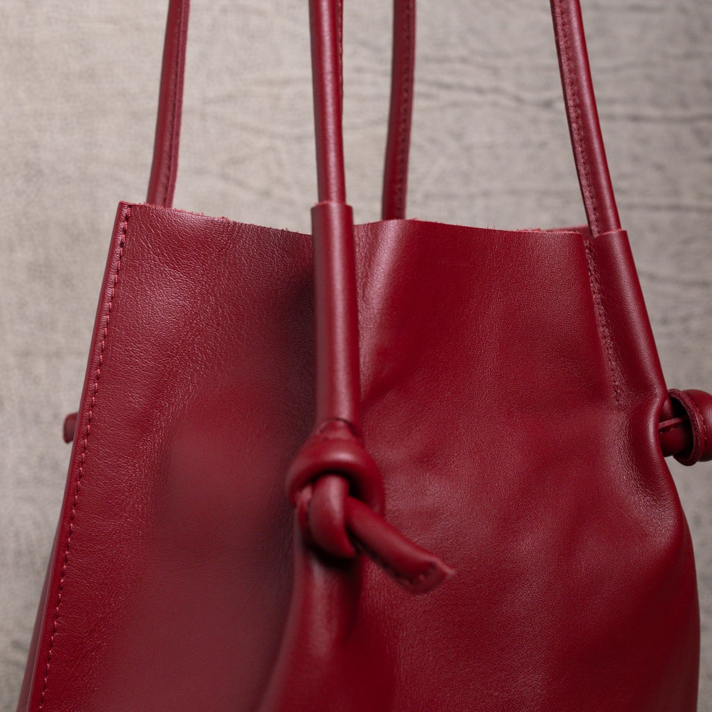 Close-up of the Flora Leather Tote in Smooth Calf Burgundy, focusing on the clean stitching, rolled handles, and knotted detail that showcase its artisanal craftsmanship.