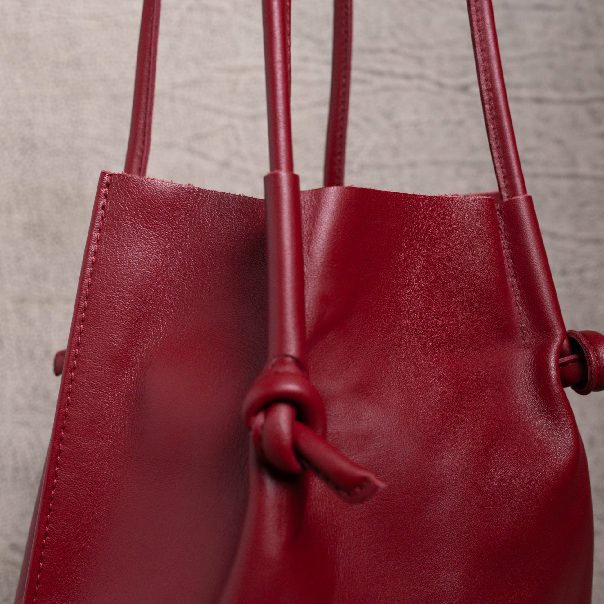 Close-up of the Flora Leather Tote in Smooth Calf Burgundy, focusing on the clean stitching, rolled handles, and knotted detail that showcase its artisanal craftsmanship.