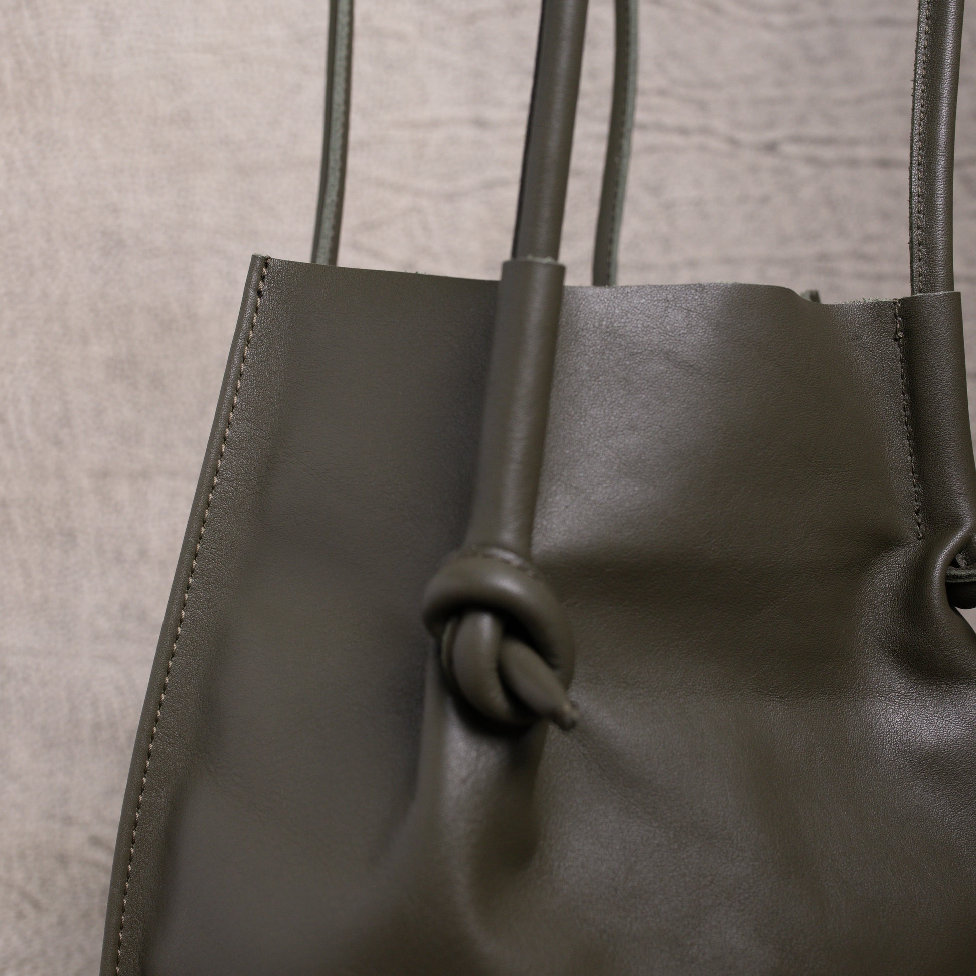 Detailed close-up of the knotted leather handle and stitching on the Flora Tote in olive green, highlighting precise craftsmanship and folded-edge finish.