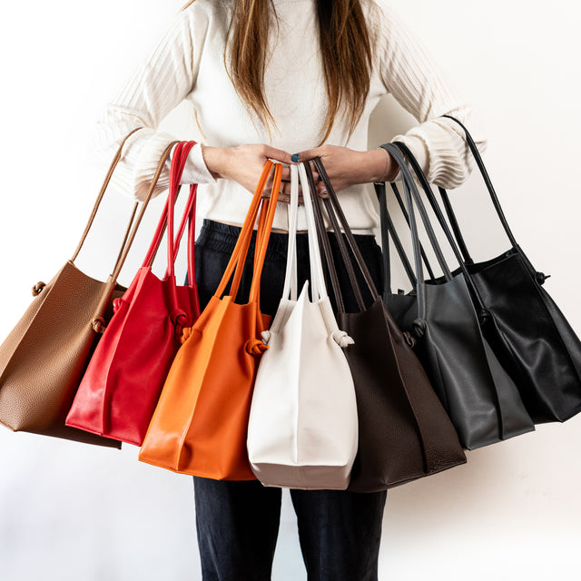 Woman holding a colorful range of Flora Leather Totes with rolled handles, raw suede interiors, and hand-finished edges—crafted for everyday carry.