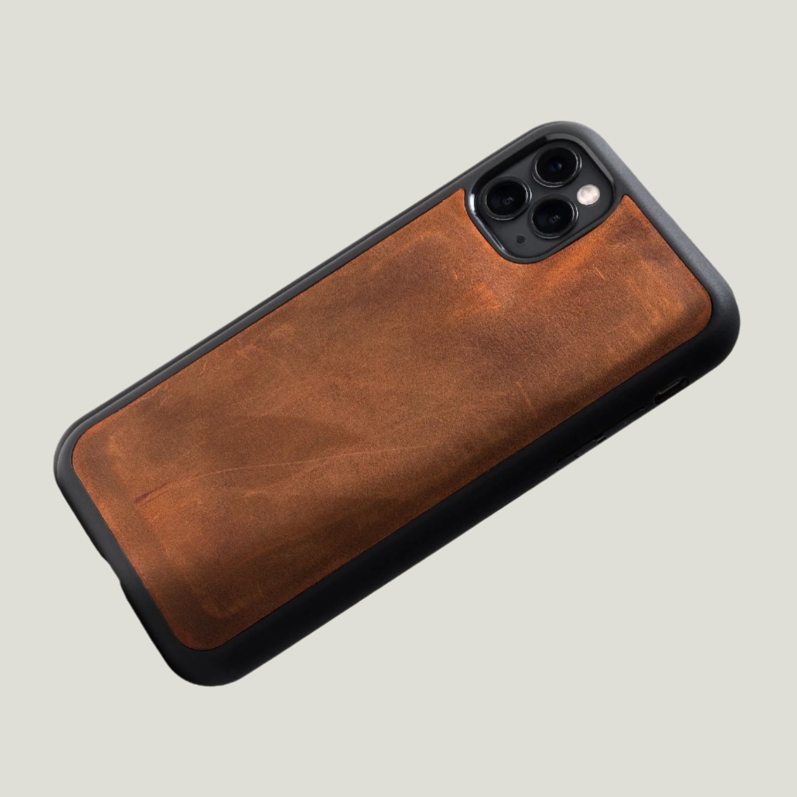 Mahogany brown leather iPhone case with black bumper frame and camera cutout, showcasing the detachable back cover design.