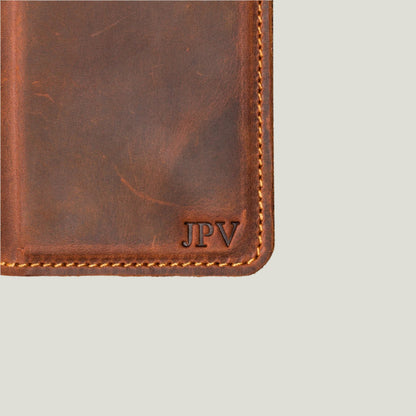 Detail view of mahogany leather iPhone wallet case with custom embossed initials 'JPV' and contrast stitching along the edge.
